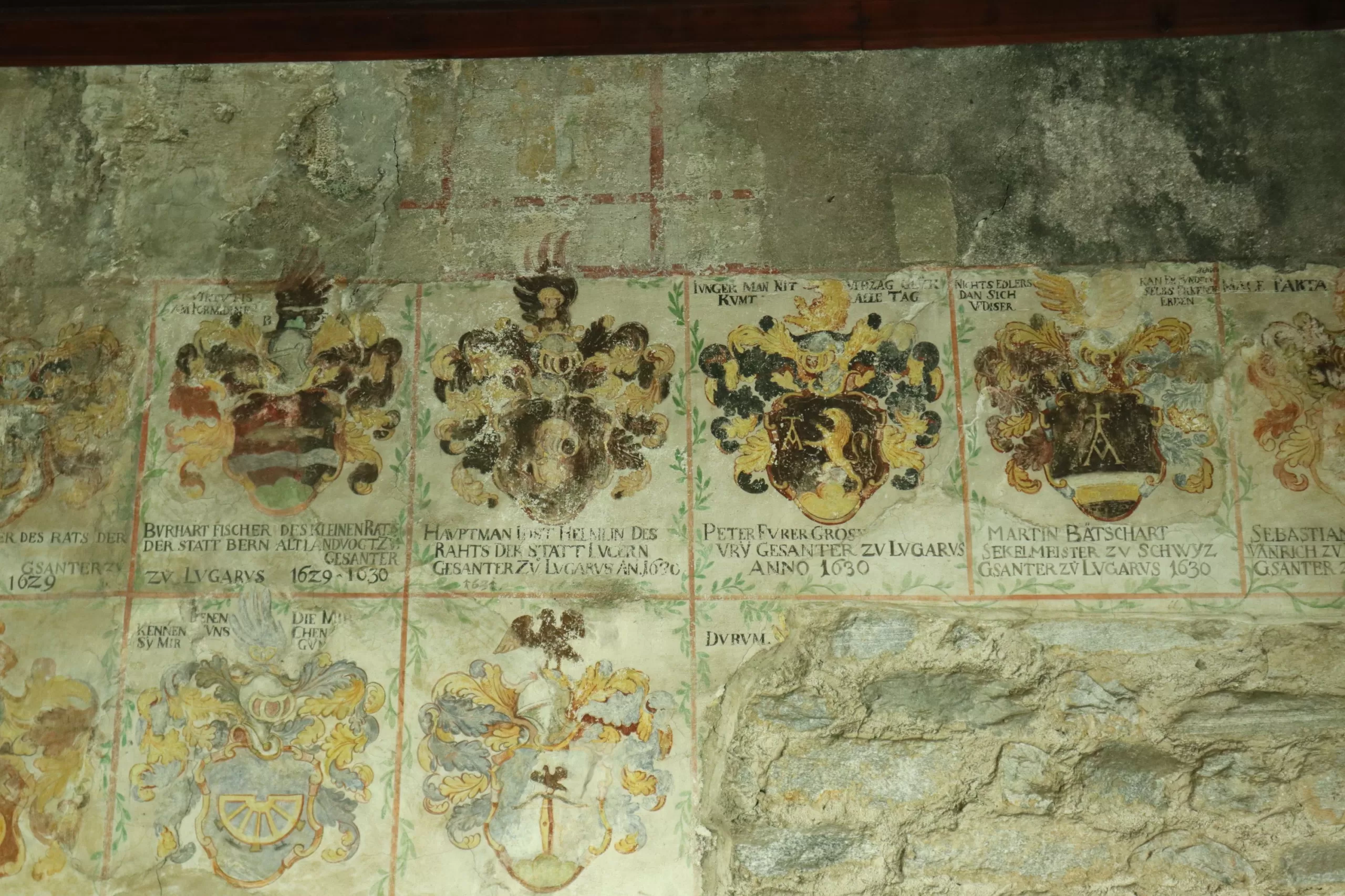 Detailaufnahme einer Wand im Castello. Darauf sind Wappen zu erkennen und Inschriften.